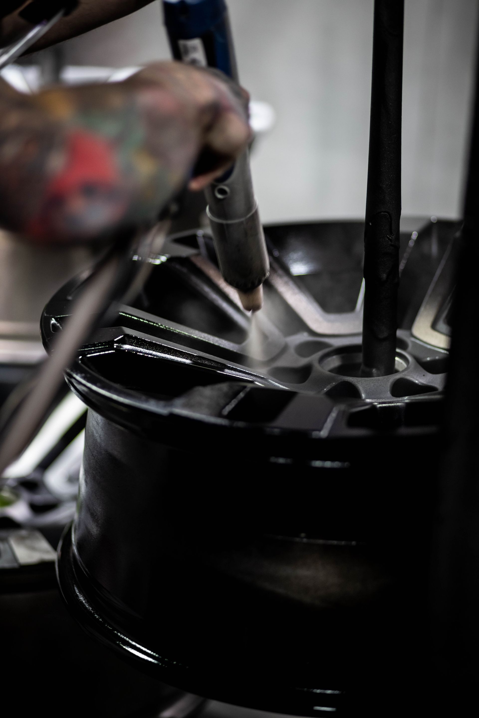 Car wheel rim being repaired by a technician with a tool in a dim workshop