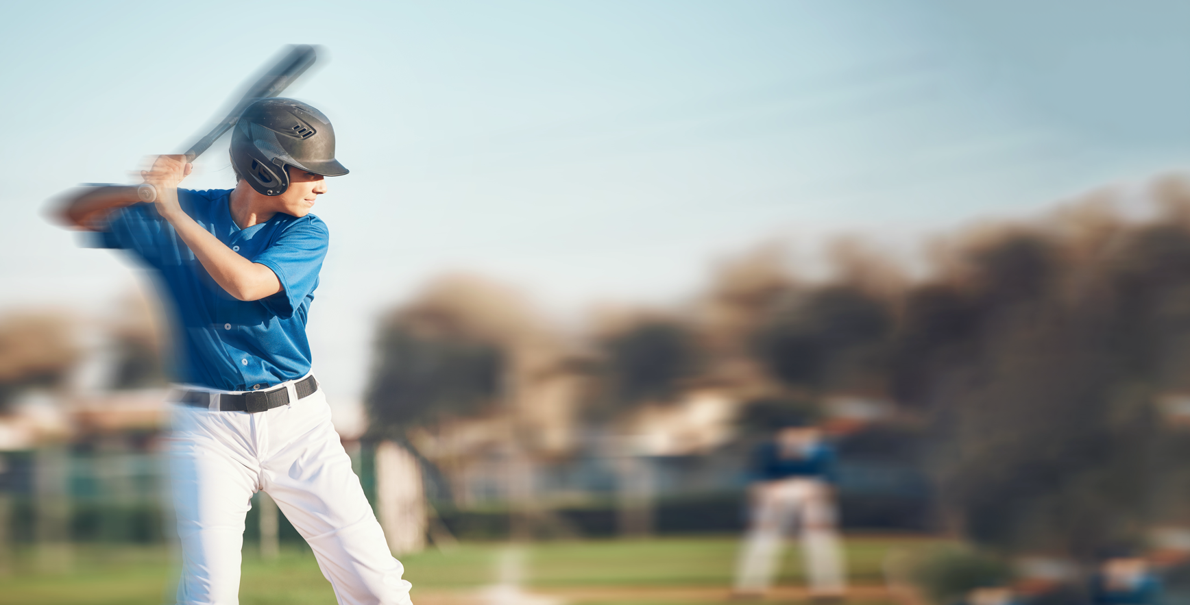 Baseball player in blue jersey and white pants swings a bat on a field, with a blurred background.