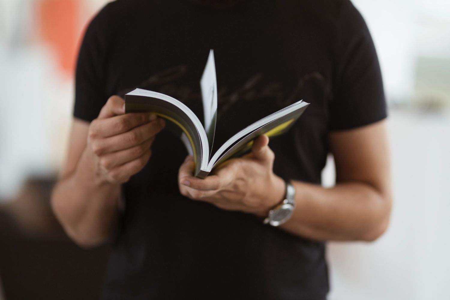 Person holding a book, flipping through the pages, wearing a black t-shirt and a watch.