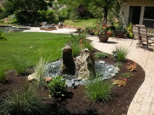 Landscaped courtyard with a stone fountain, flower beds, lawn, and patio seating