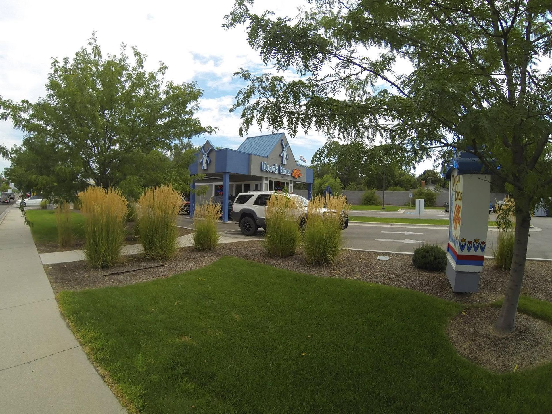Sidewalk by a grassy parking lot with trees, a blue building, and a small decorative utility box.