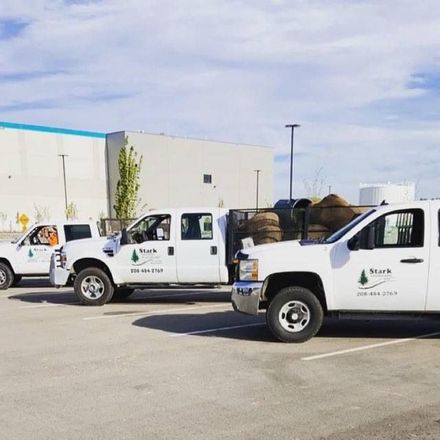 Two white utility trucks parked in a lot beside a warehouse on a sunny day