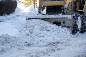 Snowplow clearing a snowy street, pushing snow with a front blade near parked cars.