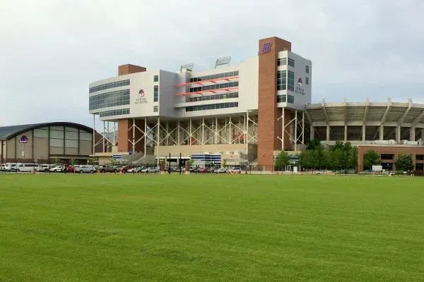 Large stadium with a green field and a modern building behind it under a cloudy sky