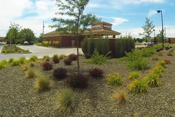 Landscaped parking lot with shrubs and a brown building under a partly cloudy sky