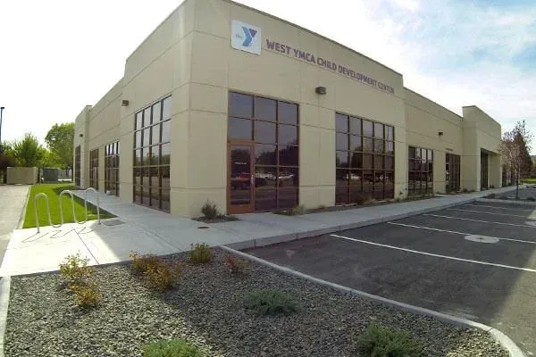 Exterior of a beige YMCA building with large windows and parking lot in front