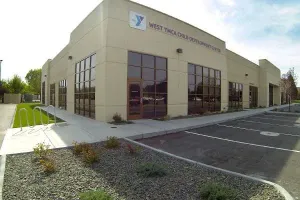 Exterior of a beige YMCA building with large windows and parking lot in front