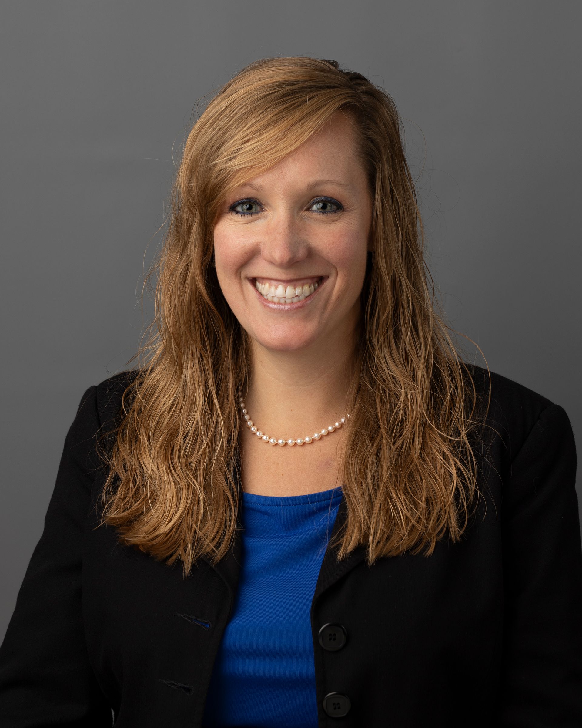 a woman in a blue shirt and black jacket is smiling for the camera .