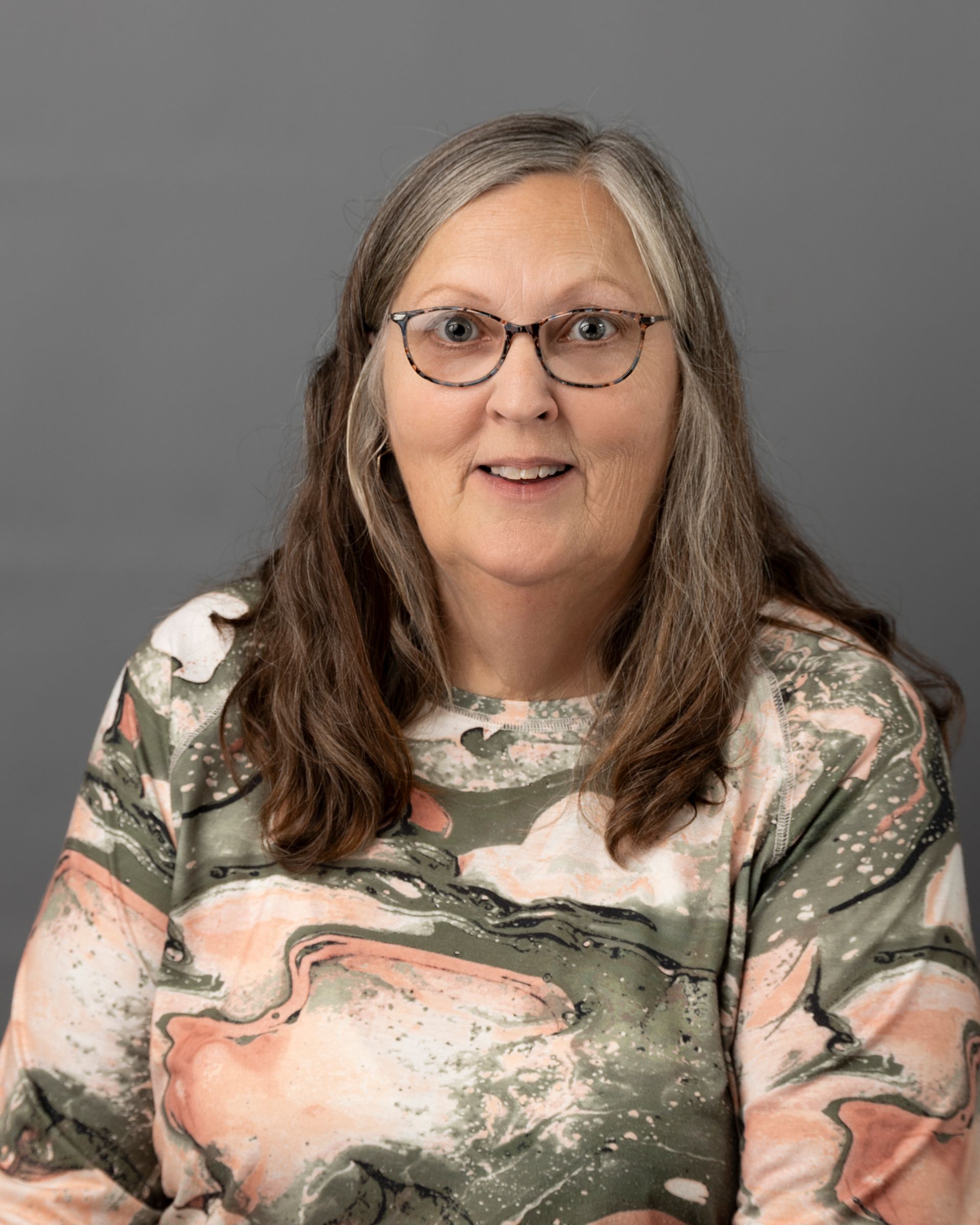 a woman wearing glasses and a pink and green sweater is smiling for the camera .