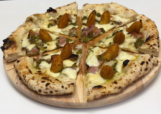 Pizza con condimenti e crocchette di patate croccanti, tagliata a fette e servita su un tagliere di legno.