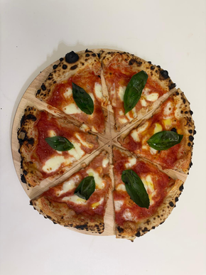 Pizza con salsa di pomodoro, mozzarella e basilico su un tagliere di legno, tagliata in sei pezzi.
