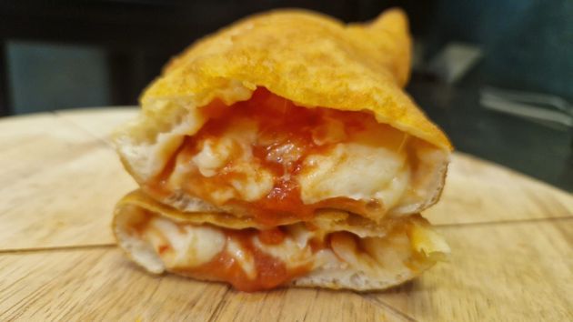 Pasta per pizza fritta, farcita con mozzarella e salsa di pomodoro, su un tagliere di legno.