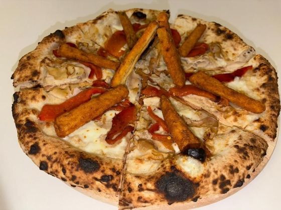 Pizza con patatine dolci, peperoni rossi e quello che sembra pollo grigliato, su una superficie bianca.