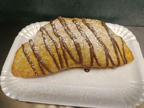 Pasta fritta ricoperta di cioccolato e spolverata di zucchero a velo, su un piatto di carta bianco.