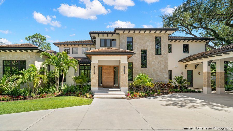 Modern two-story stone house with a front porch, driveway, and landscaped garden under a blue sky