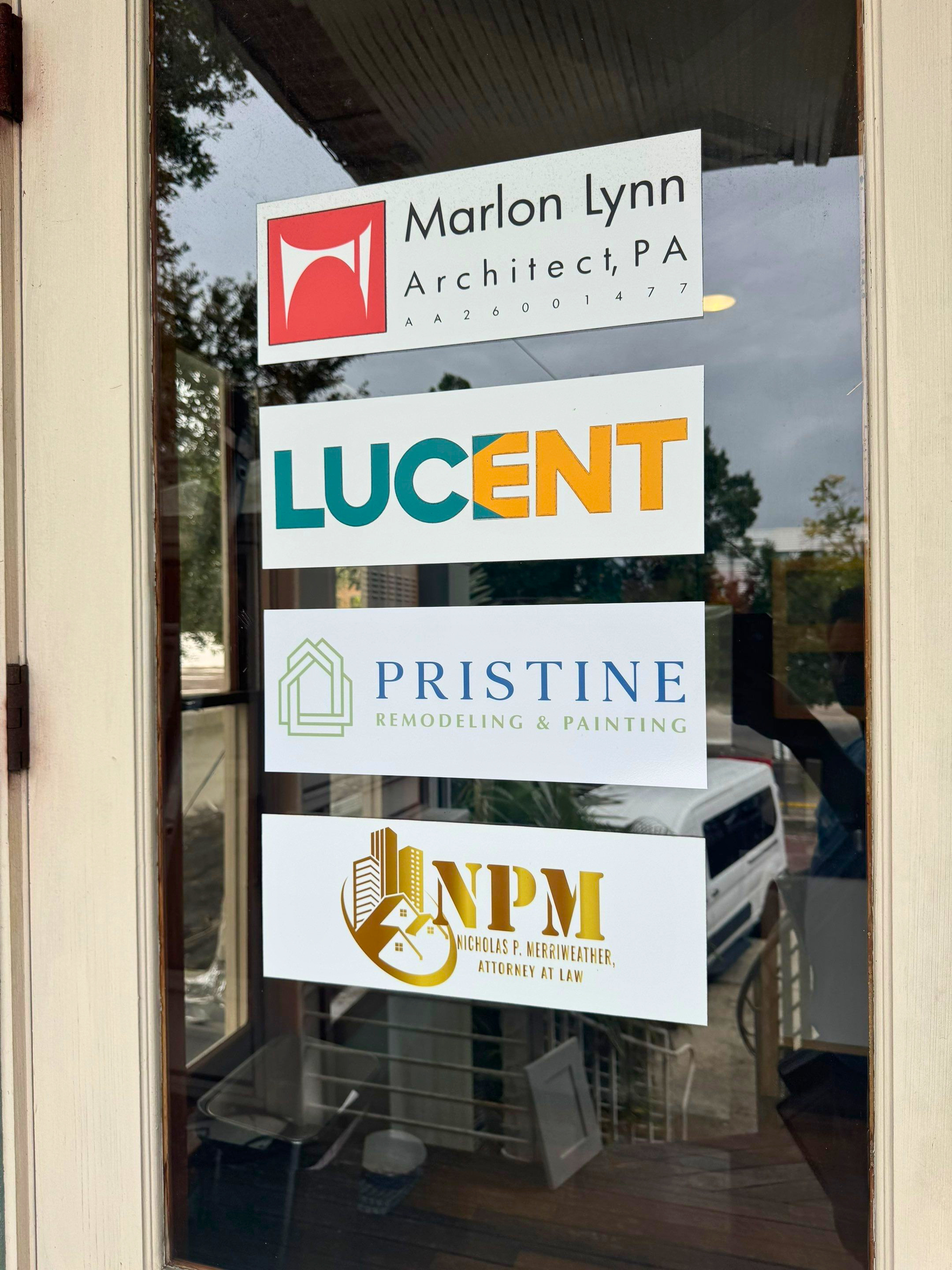 Business office window with stacked signs for Marlon Lynn Architects, Lucent, Pristine, and NPM