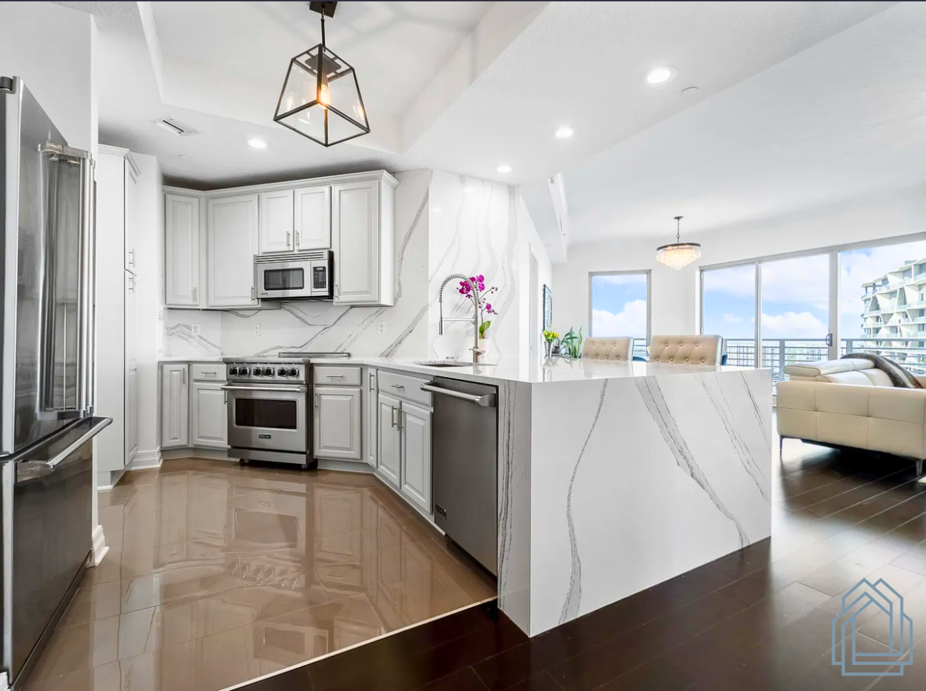 Modern open-plan kitchen with gray cabinets, marble island, stainless appliances, and bright living room views