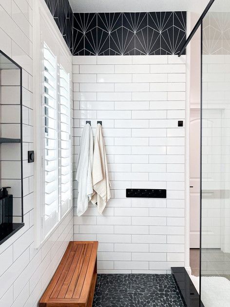 Modern shower with white subway tile, black accents, towel hooks, and a wooden bench