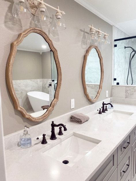 Bright modern bathroom with double sinks, oval mirrors, white countertop, and black fixtures
