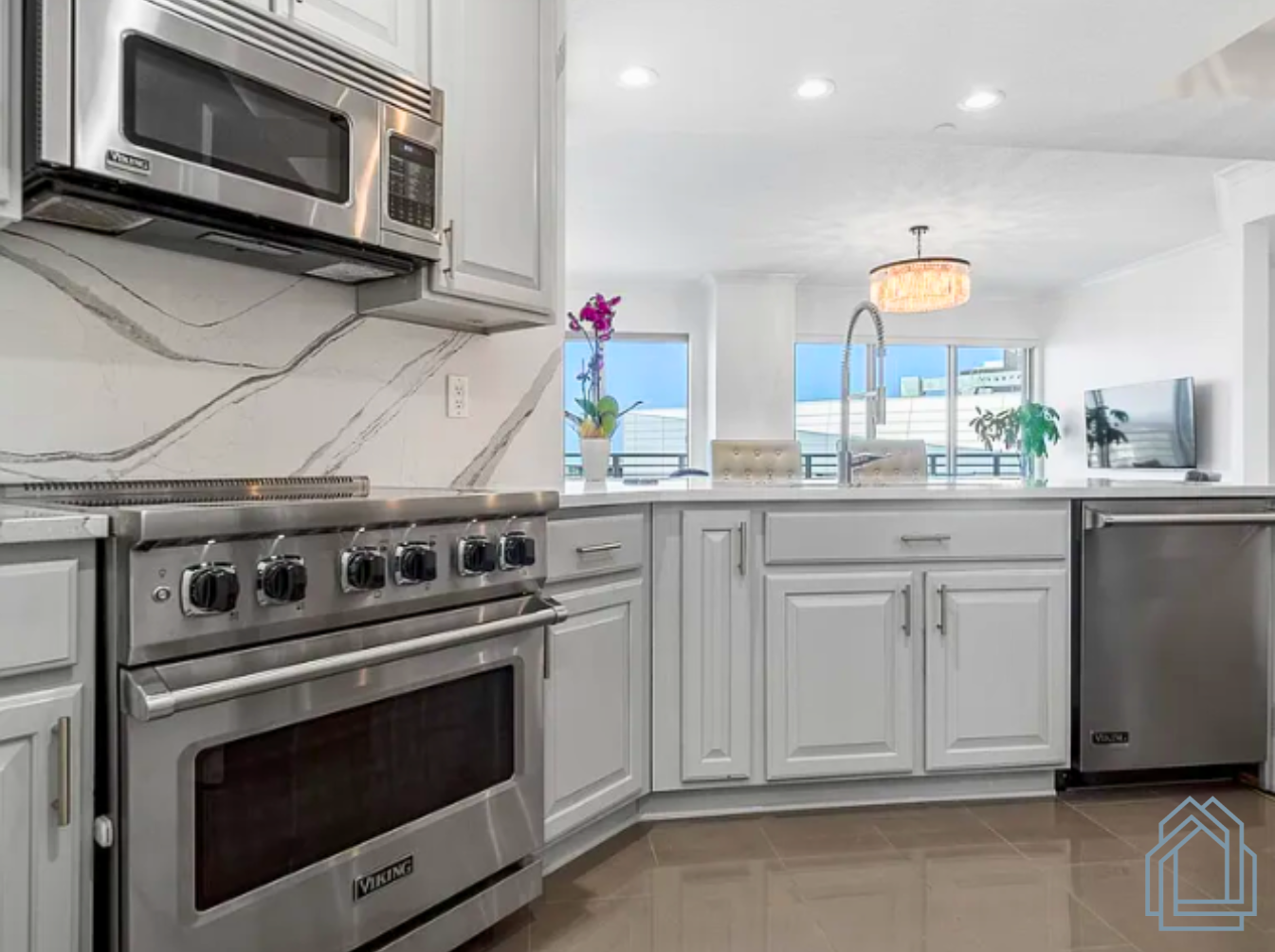 Bright modern kitchen with stainless steel appliances, white cabinets, and marble backsplash, open to a sunlit room