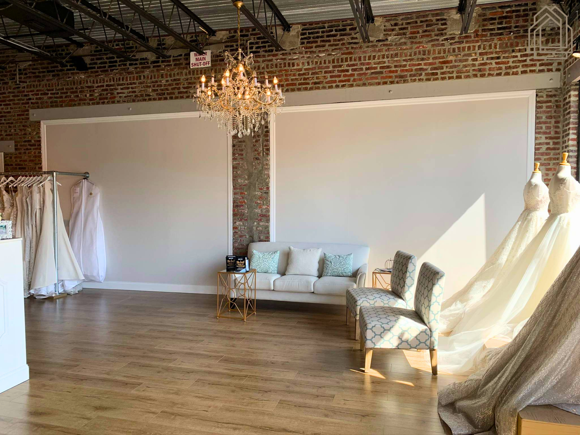 Bright loft studio with brick walls, chandelier, white sofas, and draped fabric by large windows