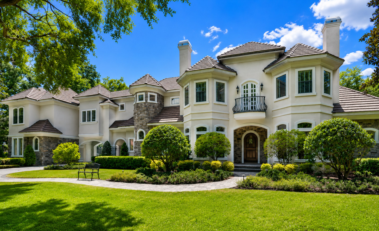 Large beige stucco mansion with arched windows, manicured lawn, and palm trees under a blue sky