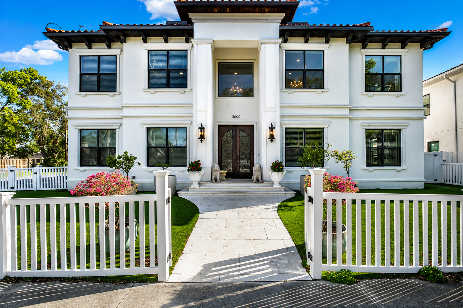 Modern two-story stone house with a front entry, driveway, and landscaped yard under a blue sky