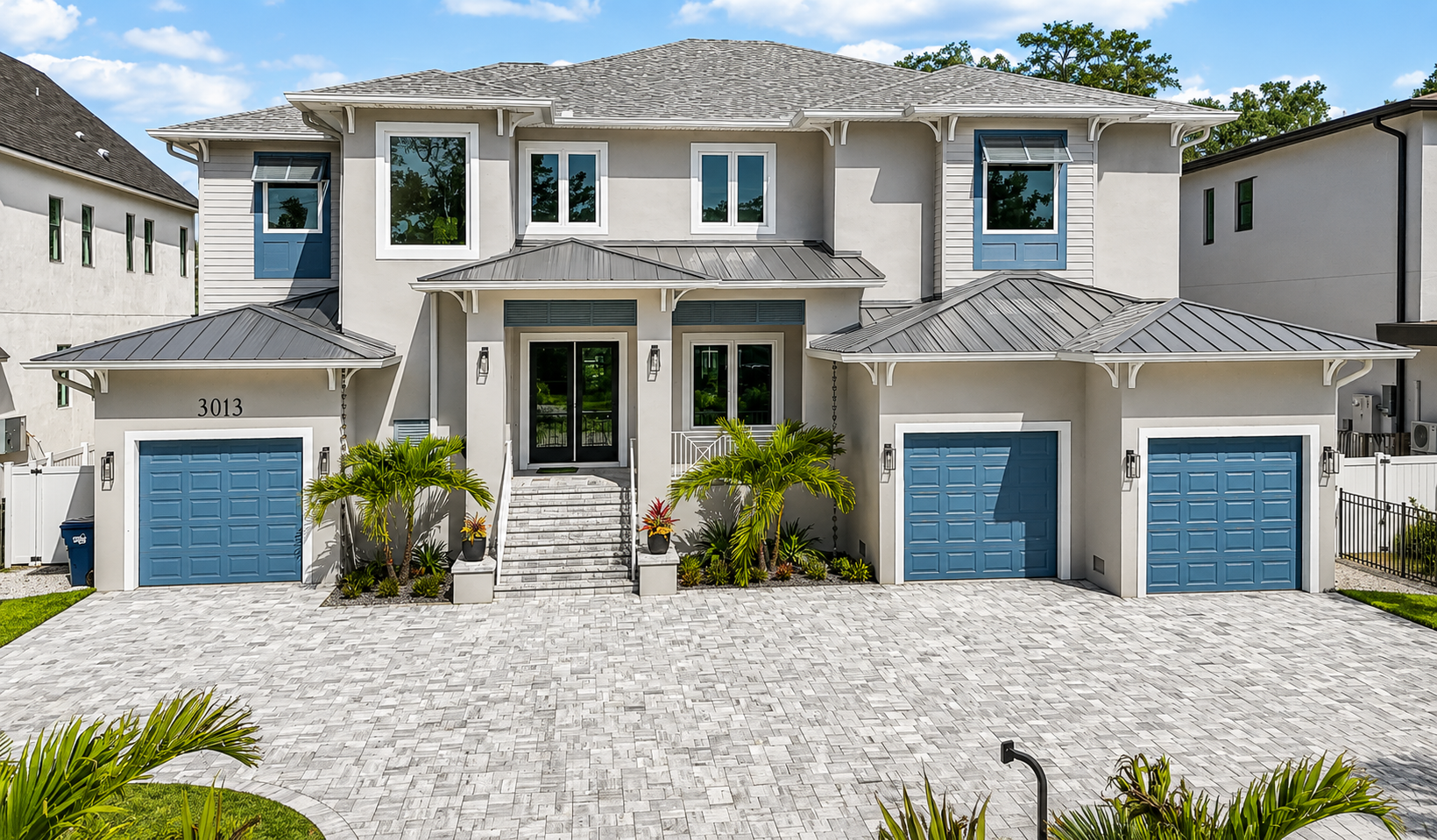 Luxury two-story white house with three blue garage doors and stone driveway