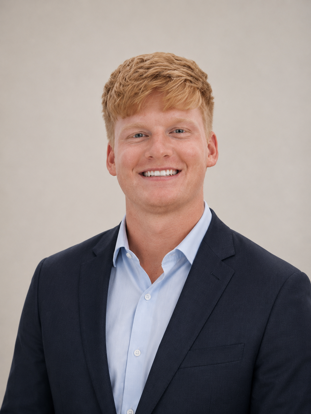 Smiling person in a navy blazer and light blue shirt against a plain background