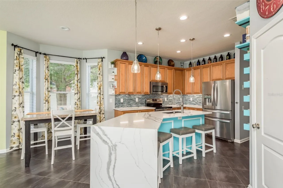 Bright modern kitchen with white island, turquoise stools, wood cabinets, and stainless steel appliances