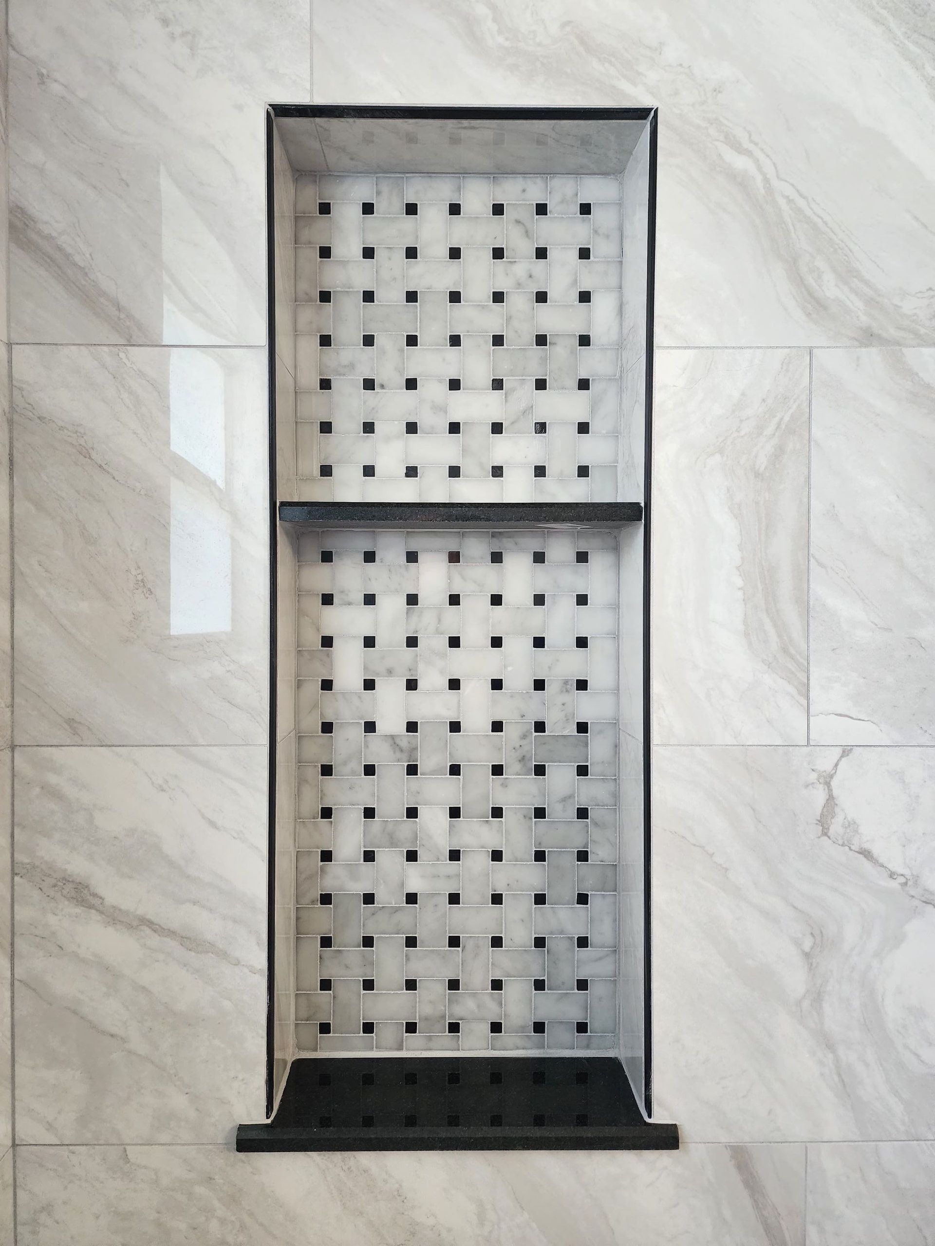 Wall-mounted metal shower shelf with perforated panels and a dark bottom ledge on tiled wall