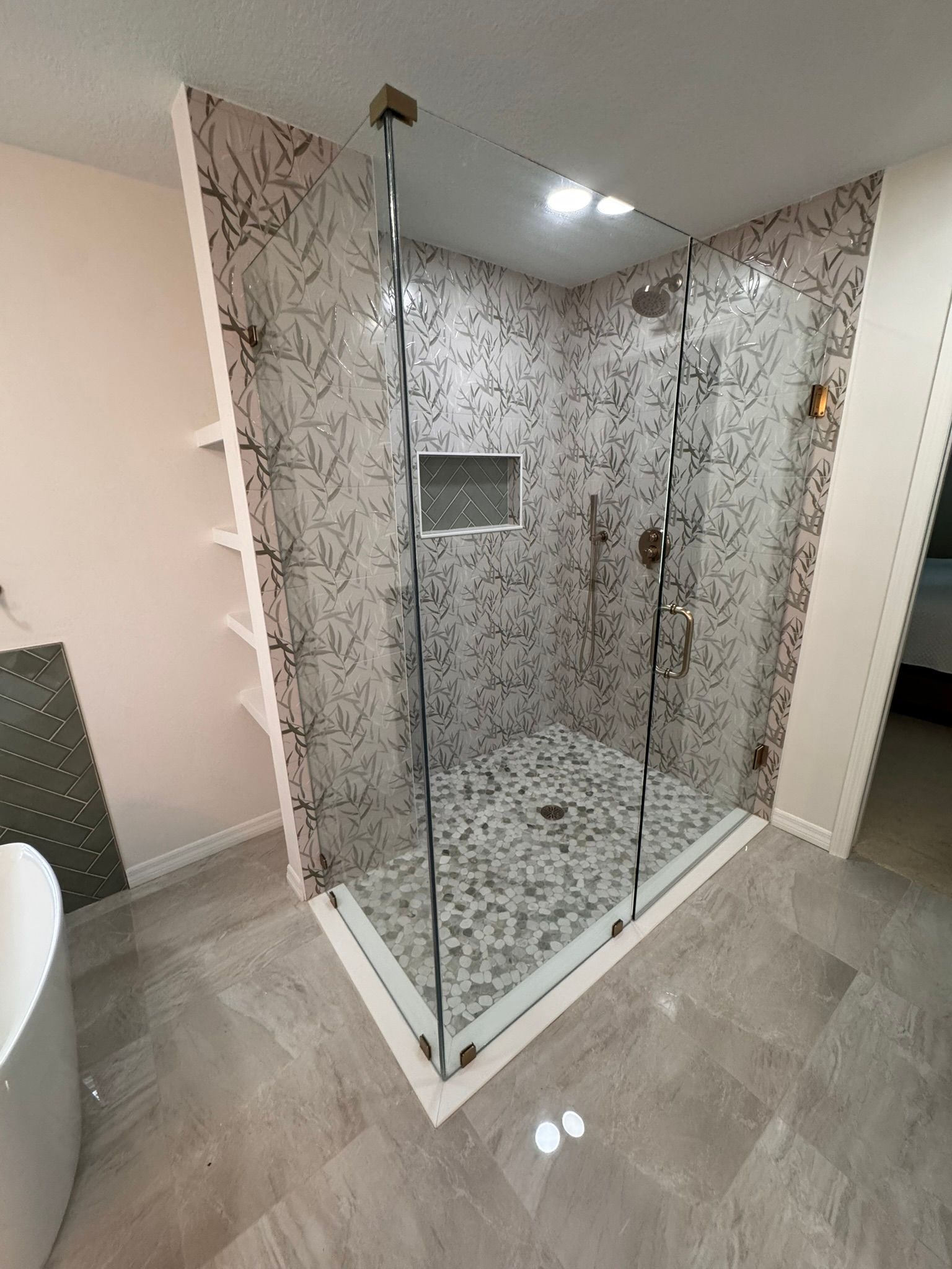 Modern glass shower enclosure with gray patterned tile walls and a built-in niche in a bathroom.