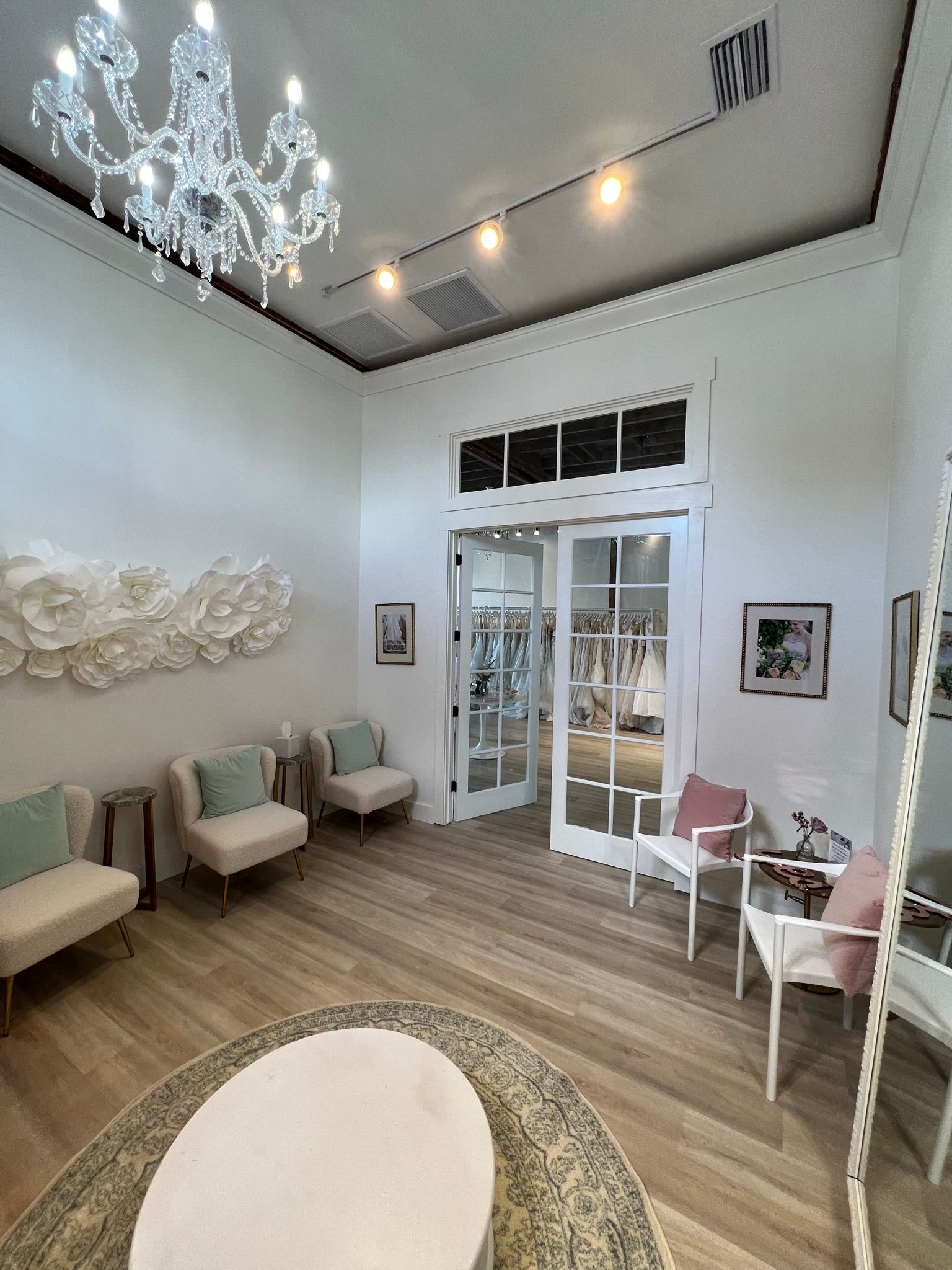 Bright boutique waiting room with cream seating, crystal chandelier, and glass doors.