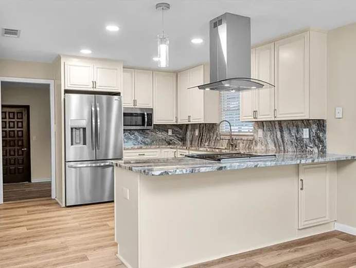 Modern kitchen with stainless steel appliances, white cabinets, island, and wood-look flooring