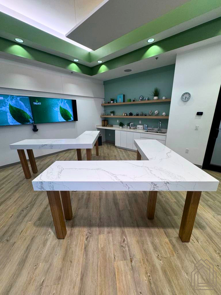 Modern classroom with white tables, wooden legs, wall-mounted screens, shelves, and green ceiling lights