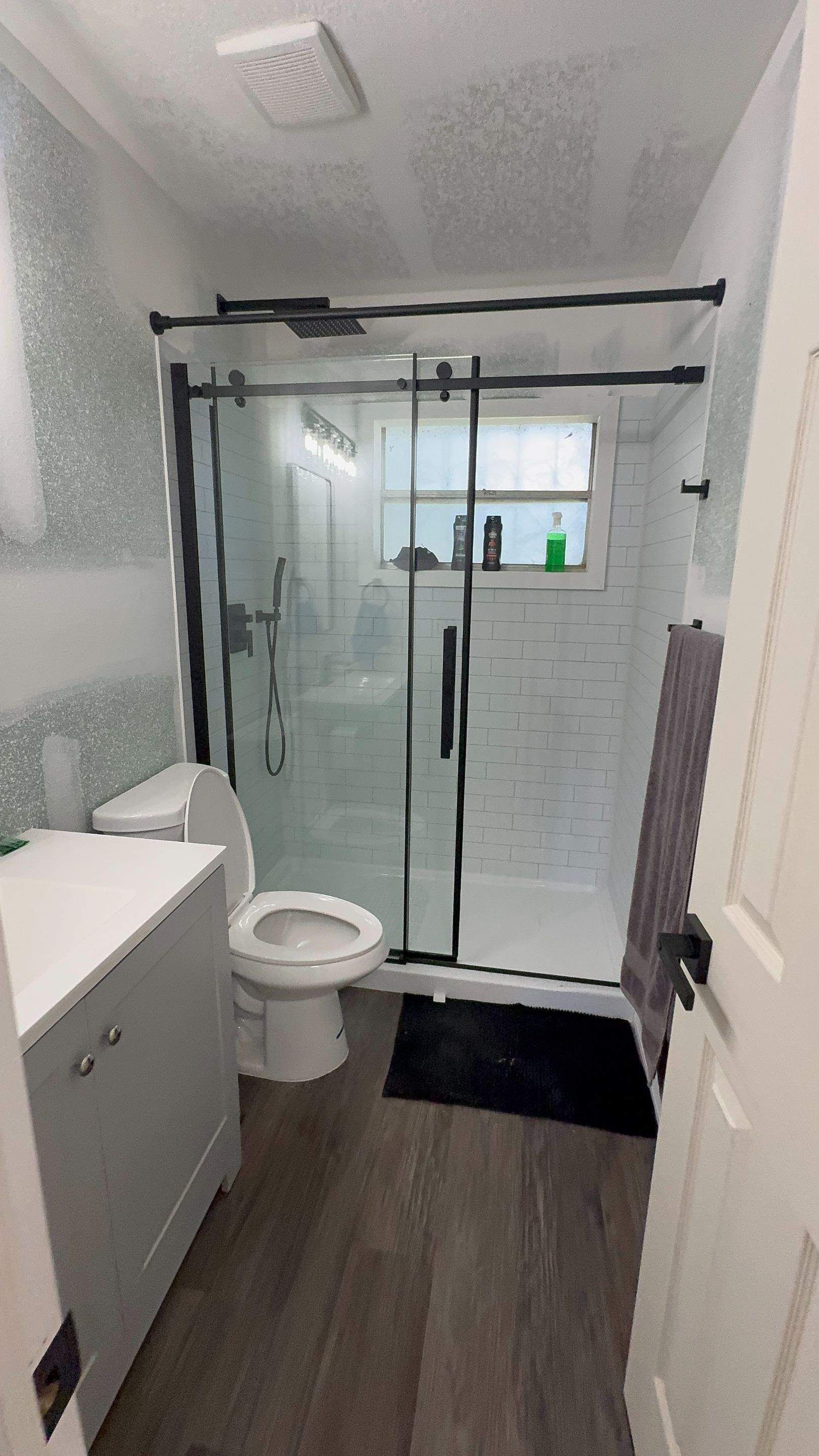 Modern bathroom with glass shower, white toilet and vanity, gray floor, and skylight ceiling light