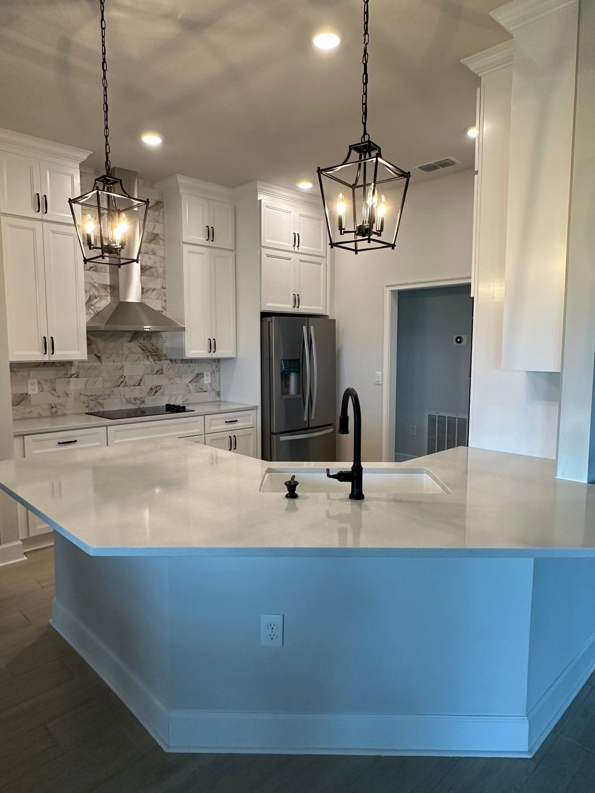 Bright modern kitchen with white cabinets, gray backsplash, stainless fridge, and a white island with black pendant lights