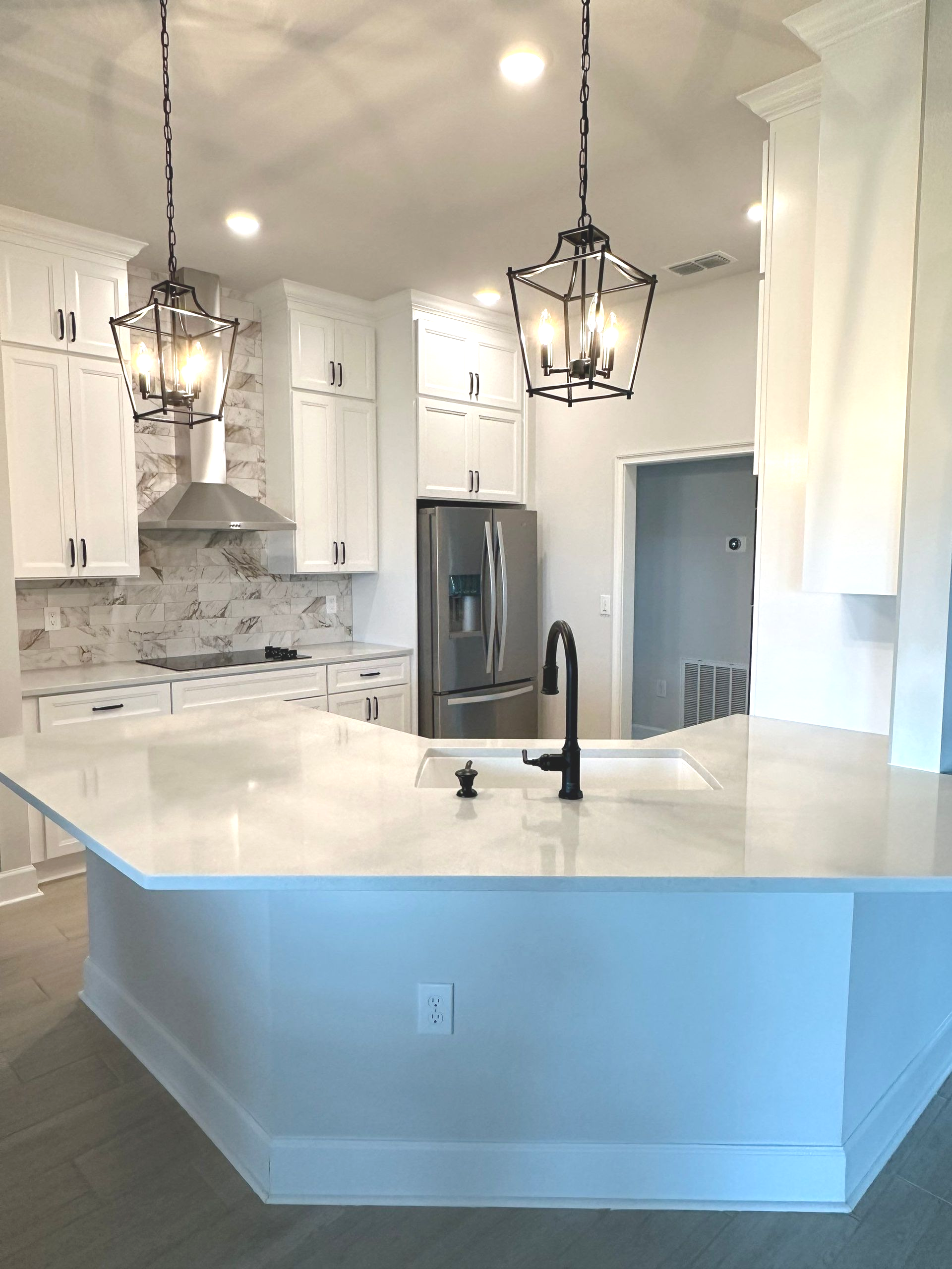 Bright modern kitchen with white cabinets, marble island, black pendant lights, and stainless steel fridge