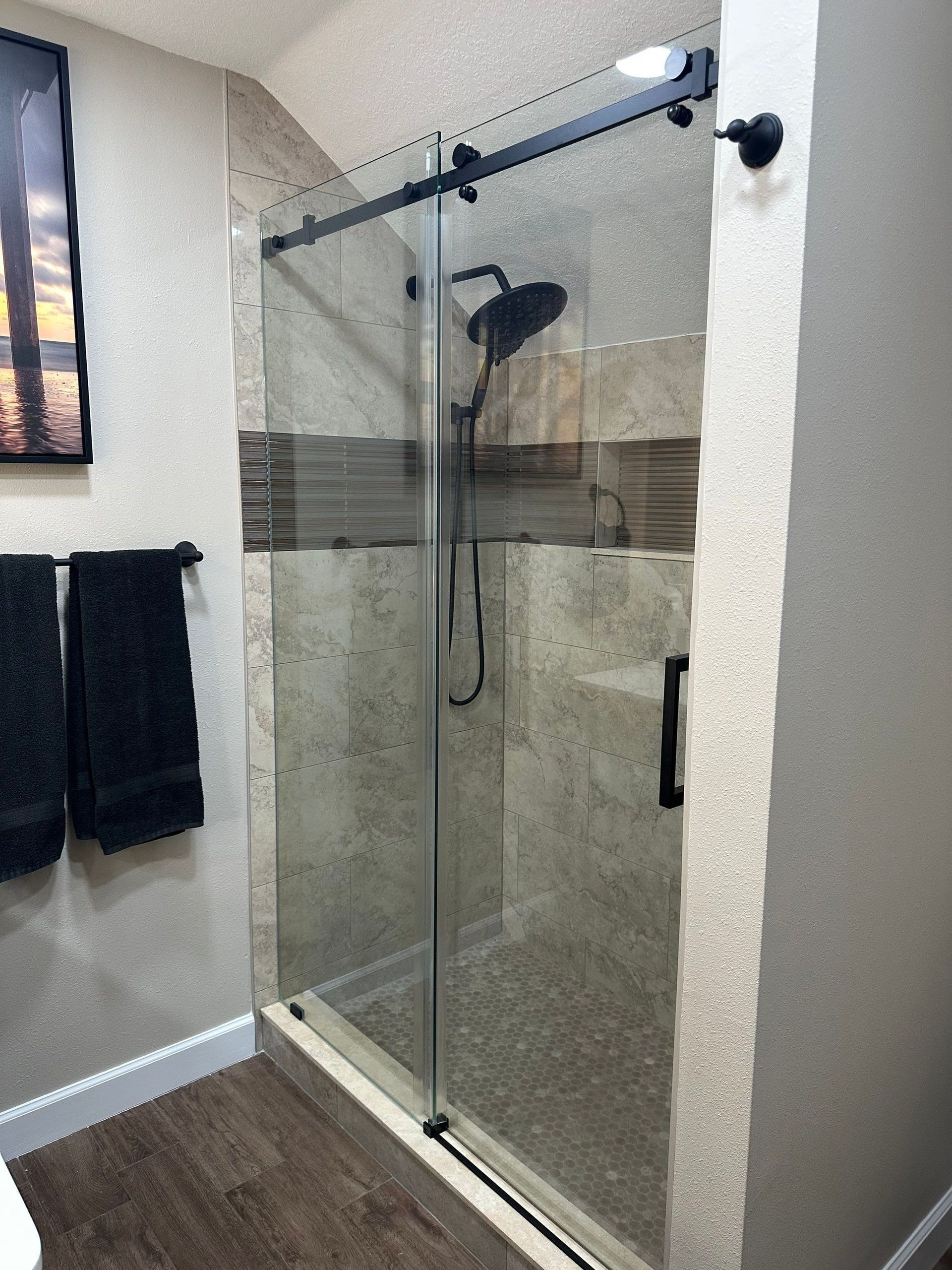 Glass walk-in shower with tiled walls, stone floor, and a black showerhead in a bathroom