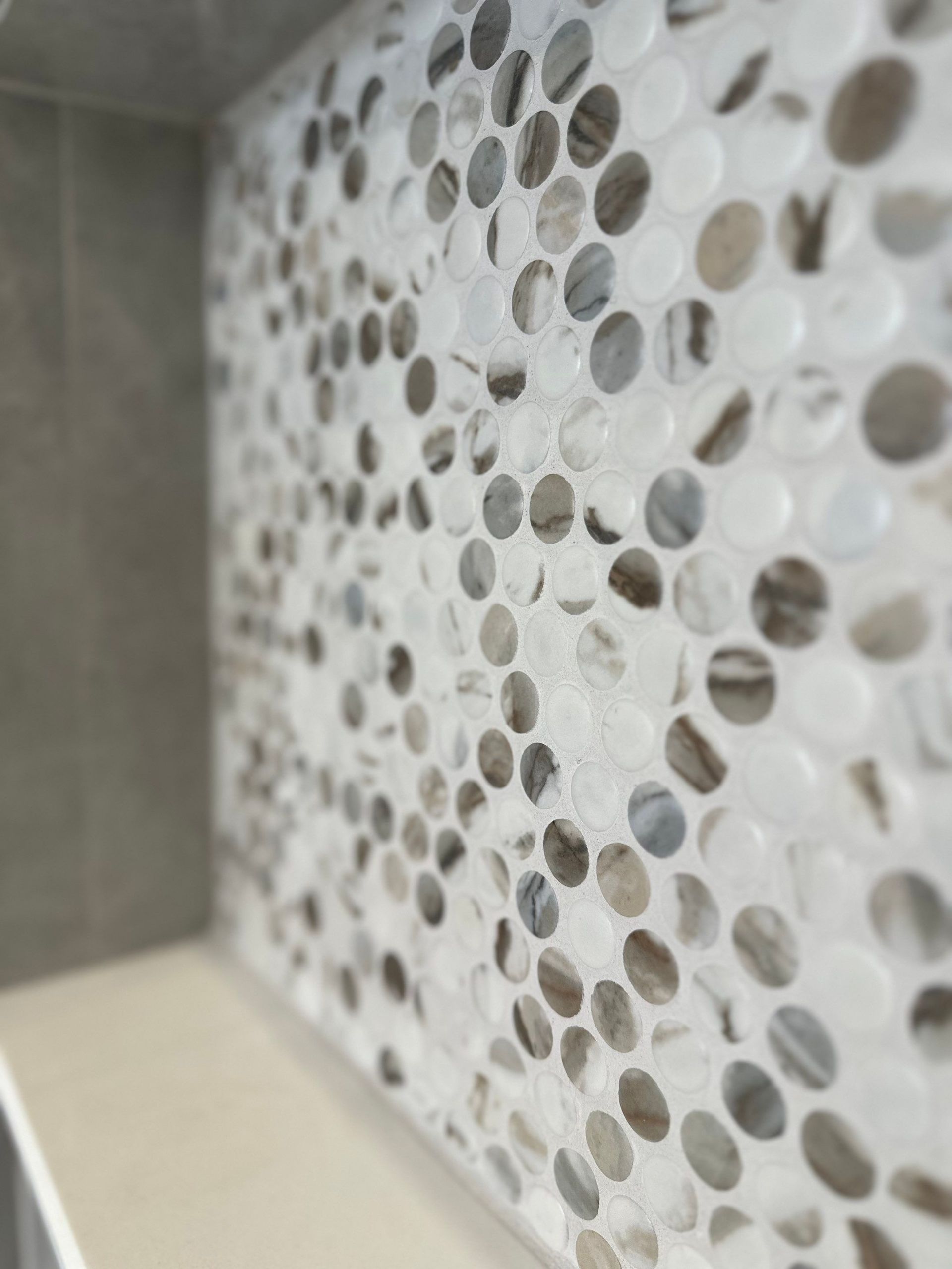 Close-up of a white and gray mosaic tile wall with circular stone accents.