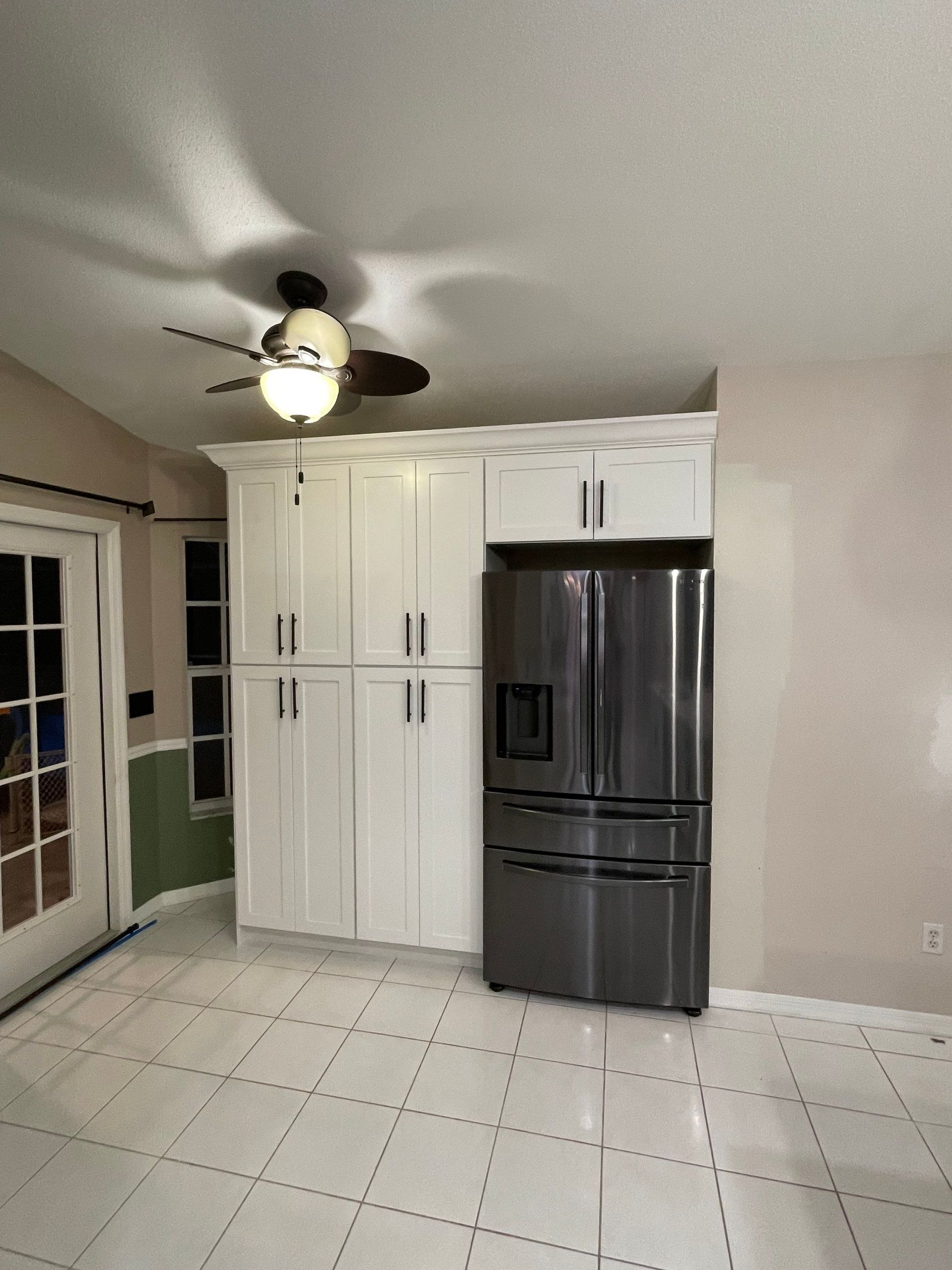 Small kitchen with white cabinets, stainless steel fridge, tiled floor, and sliding glass door.
