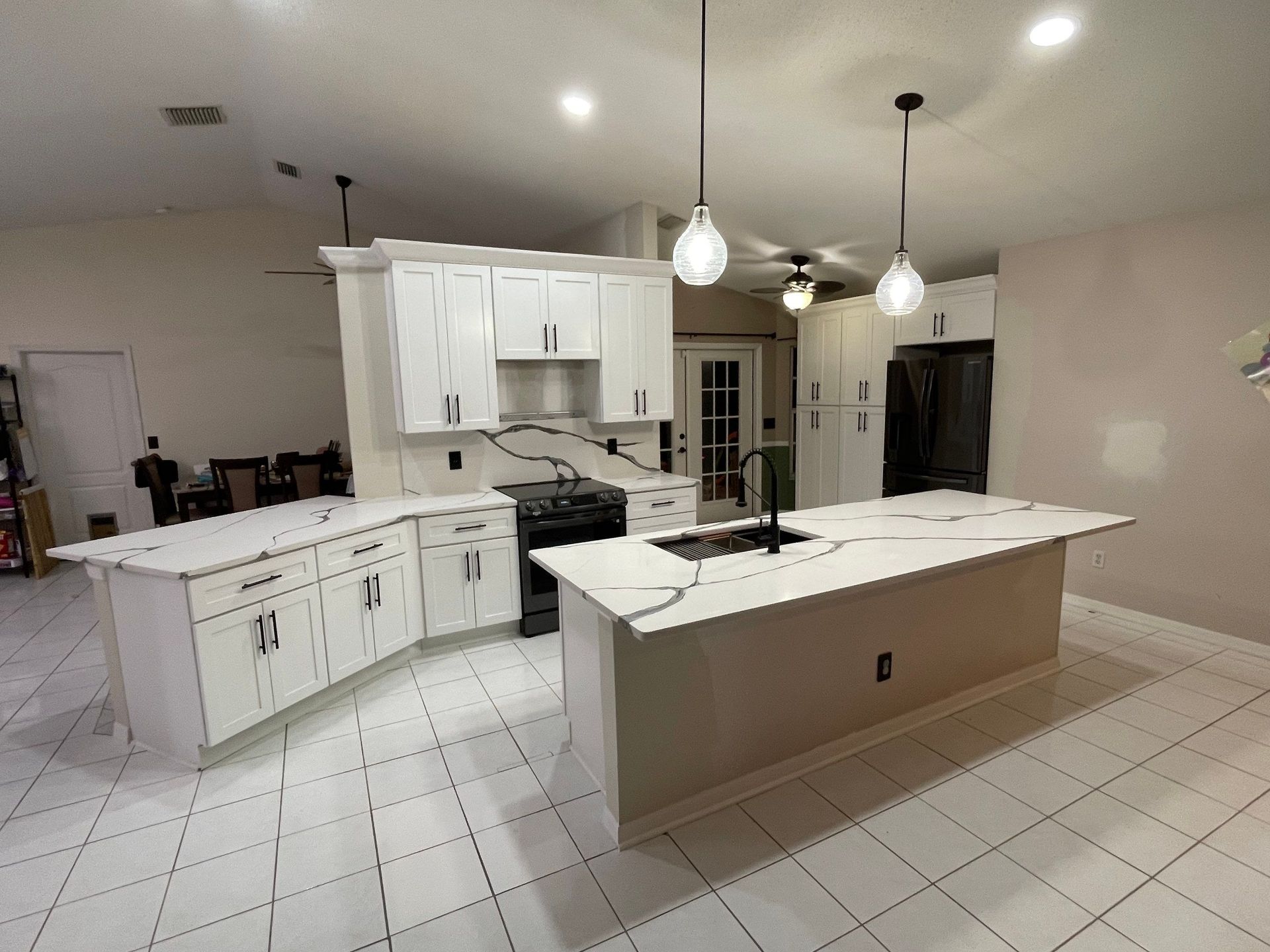 Bright kitchen with white cabinets, large island, tiled floor, and pendant lights