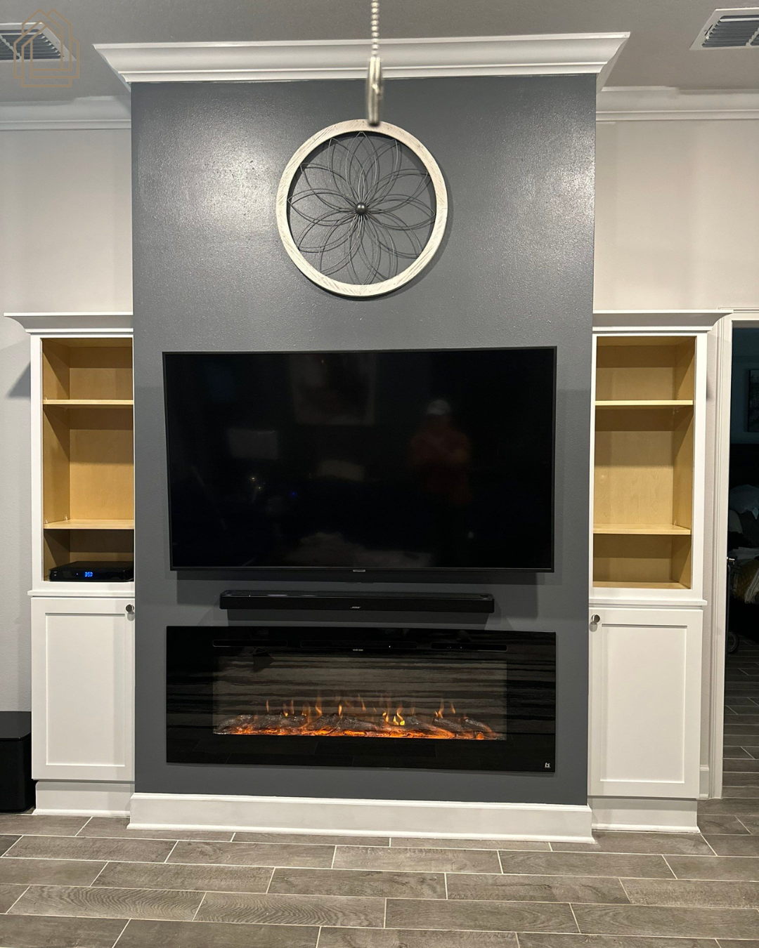 Living room wall with mounted TV, electric fireplace, and round clock between built-in shelves