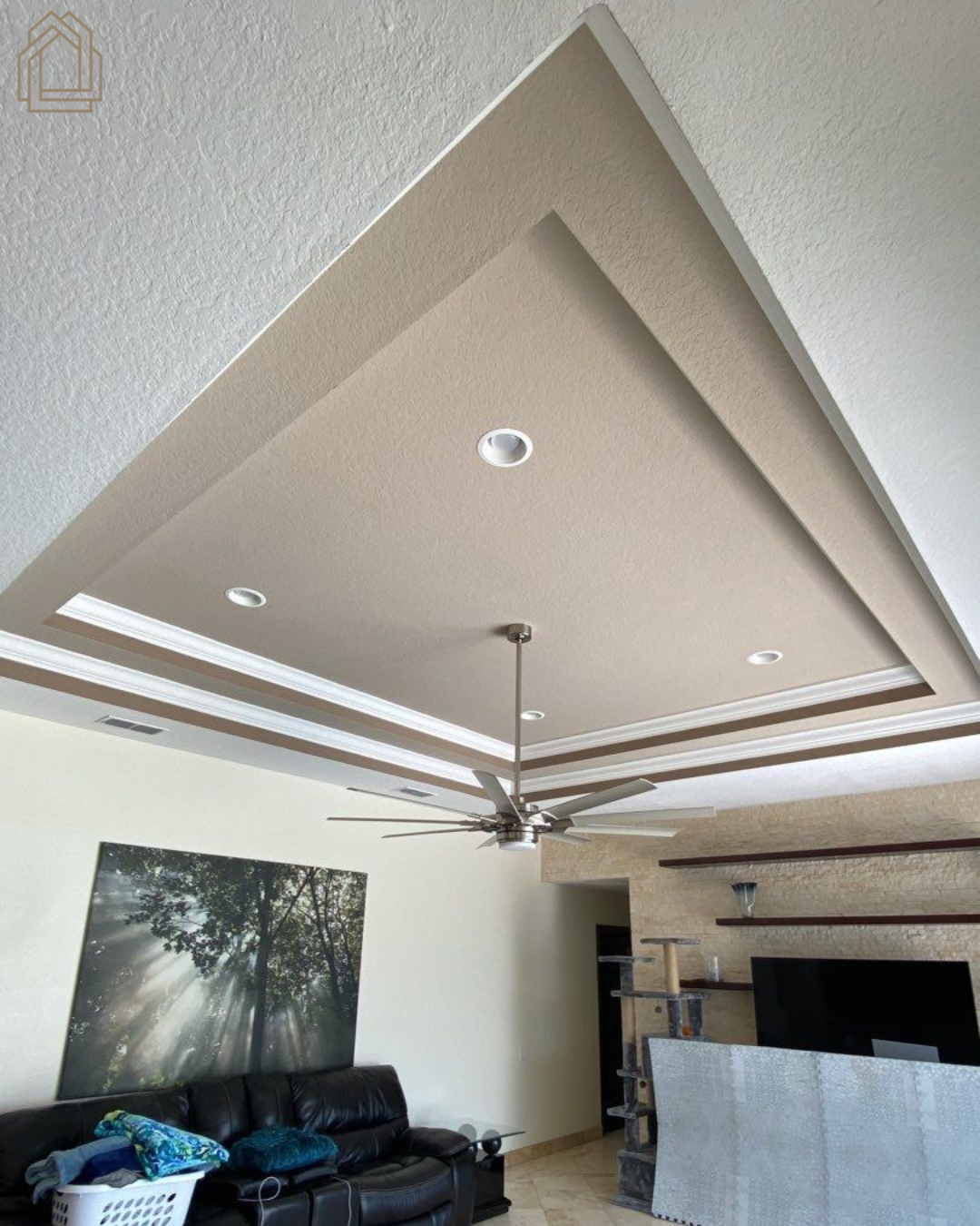 Living room with tray ceiling, ceiling fan, recessed lights, black sofa, large wall art, and TV area