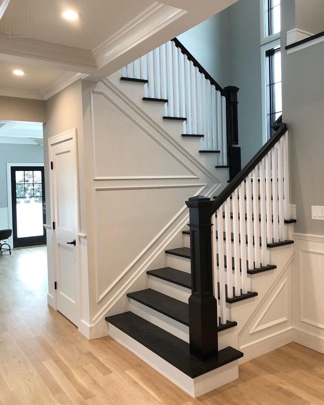 Interior staircase with black railings, gray carpeted steps, and white paneled walls in a bright hallway