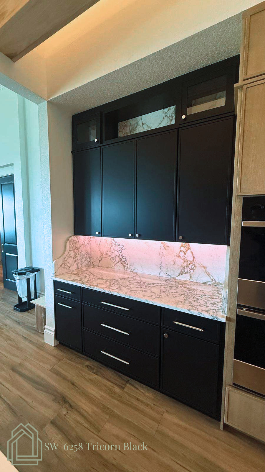 Black built-in cabinets with pink marble backsplash and wood flooring in a modern kitchen hallway