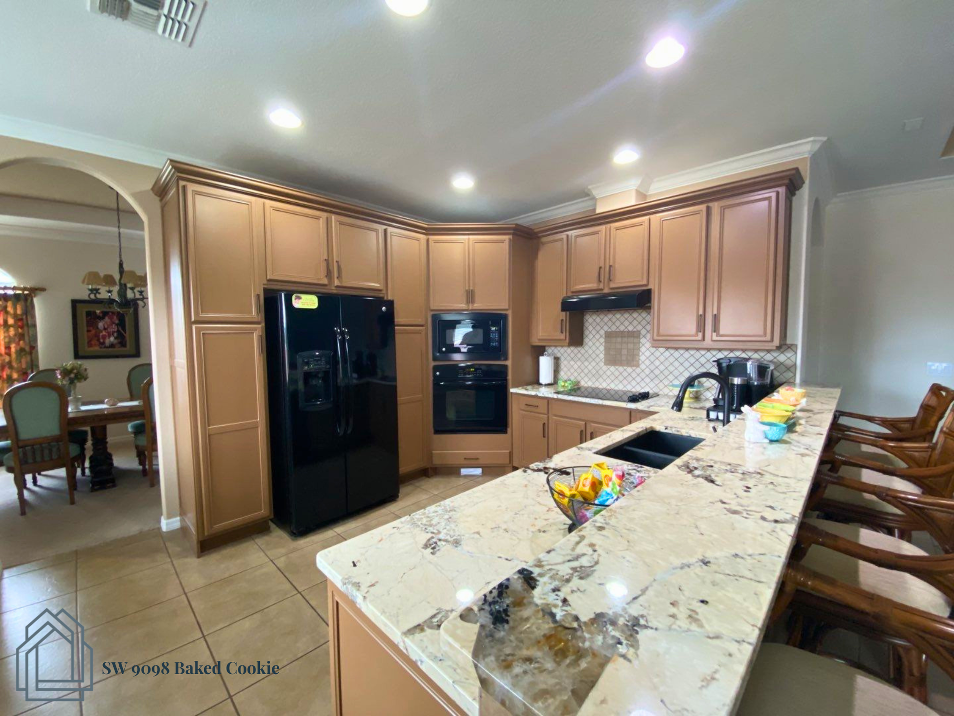 Modern kitchen with light wood cabinets, black appliances, and a granite island with fruit bowl.