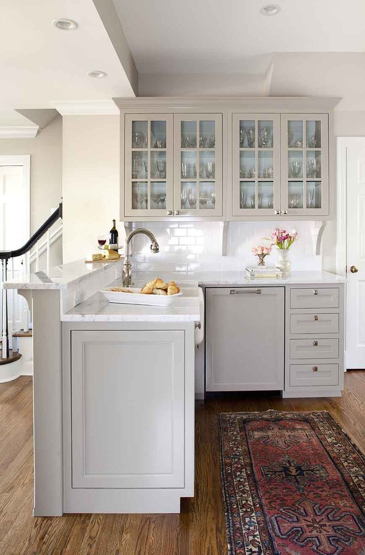 Bright white kitchen with island, glass-front cabinets, and patterned rug on wood floor