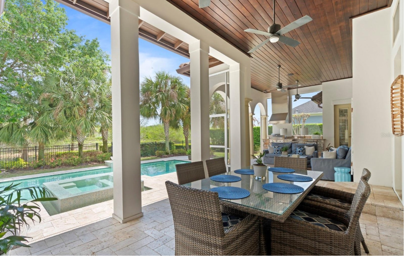 Covered patio dining area overlooking a pool and green backyard, with wicker chairs and blue table settings.