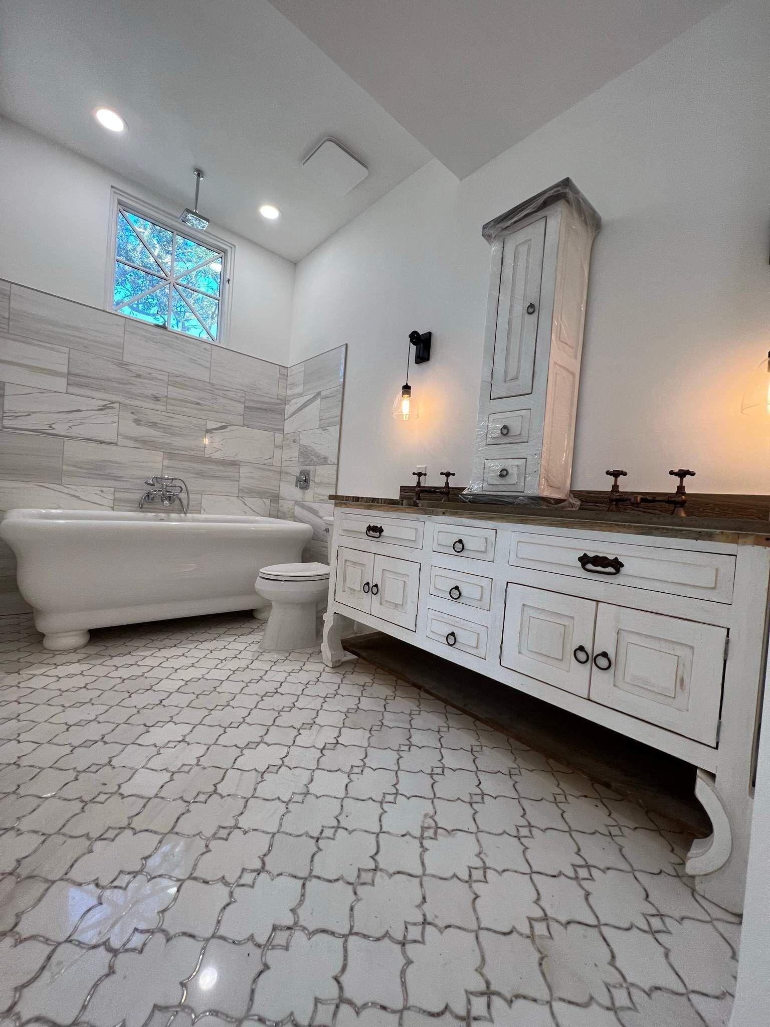 Bright white bathroom with clawfoot tub, patterned tile floor, and antique vanity under a vaulted ceiling.